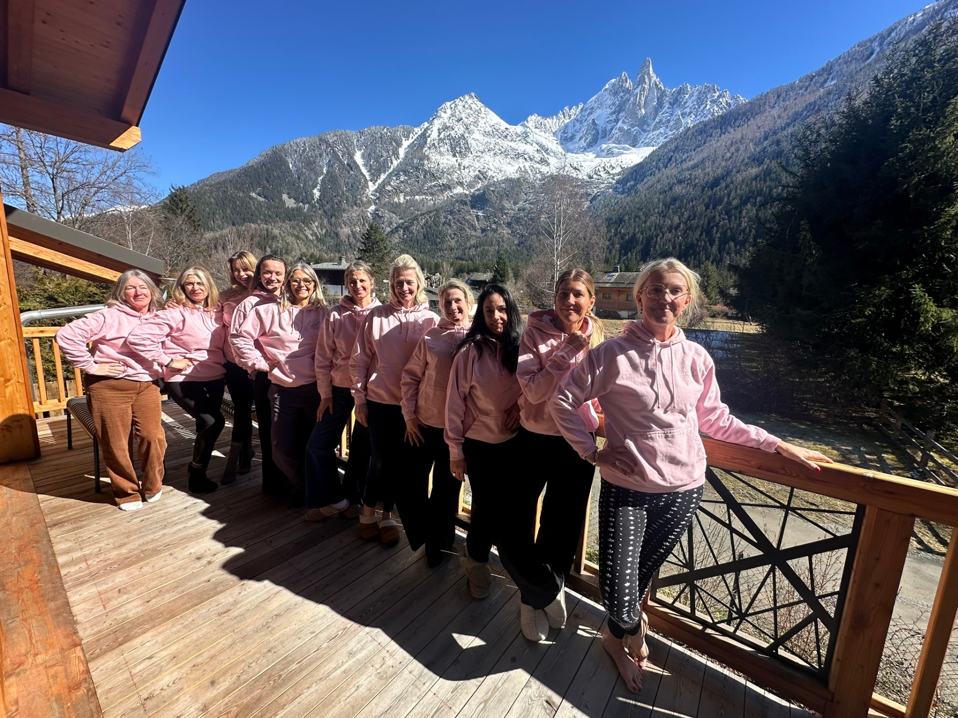 A group of women in Girl Powder hoodies on the chalet balcony with snowy peaks behind