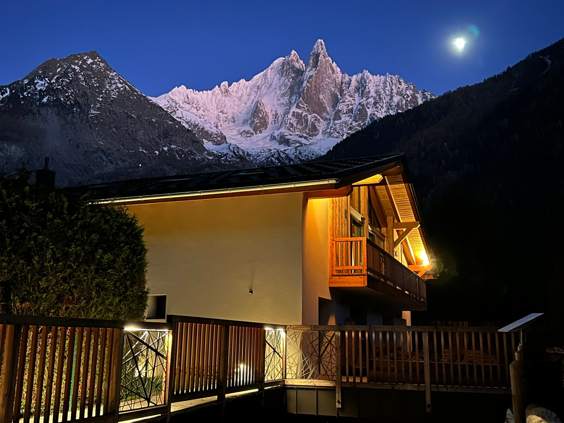 Exterior of Chalet Mélèzes with illuminated timbers and dramatic view of the Chamonix mountains at night